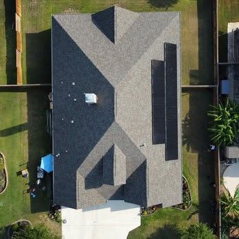 Aerial view of a house roof with gray shingles, vents, and a driveway at the bottom.