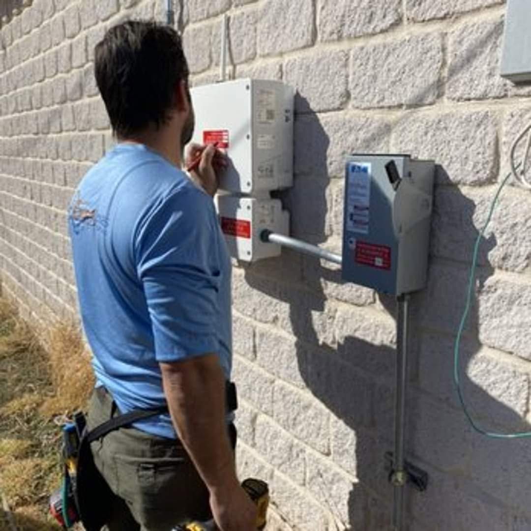 Man in blue shirt inspecting a wall-mounted electrical box on a stone exterior wall