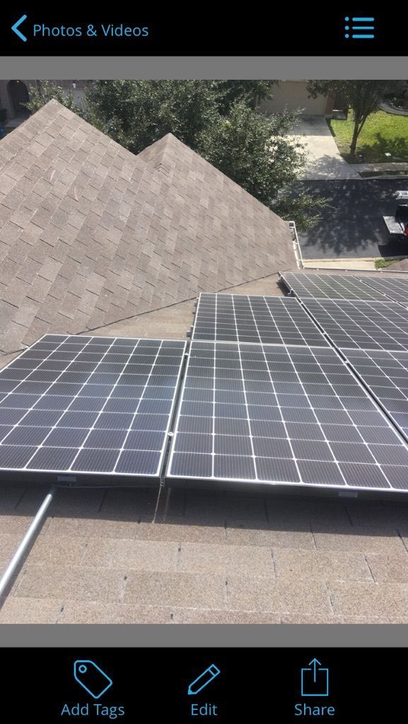 Roof-mounted solar panels on a house with neighboring rooftops and trees in the background
