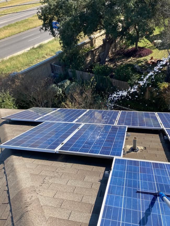 Solar panels on a rooftop beside trees and a road, with one panel partially covered by a tarp.