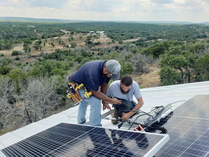 Two workers installing solar panels on a rooftop overlooking a green landscape.