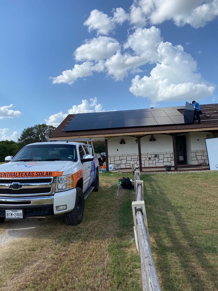 Workers on a white truck and house roof installing solar panels on a sunny day.