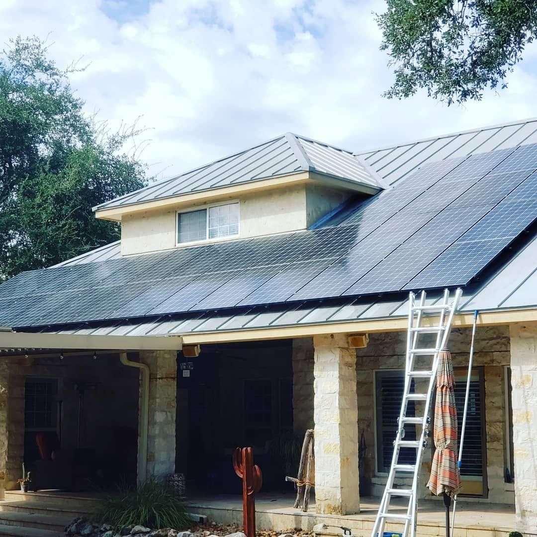 House with a metal roof under repair, with ladders leaning against the front porch and roof.
