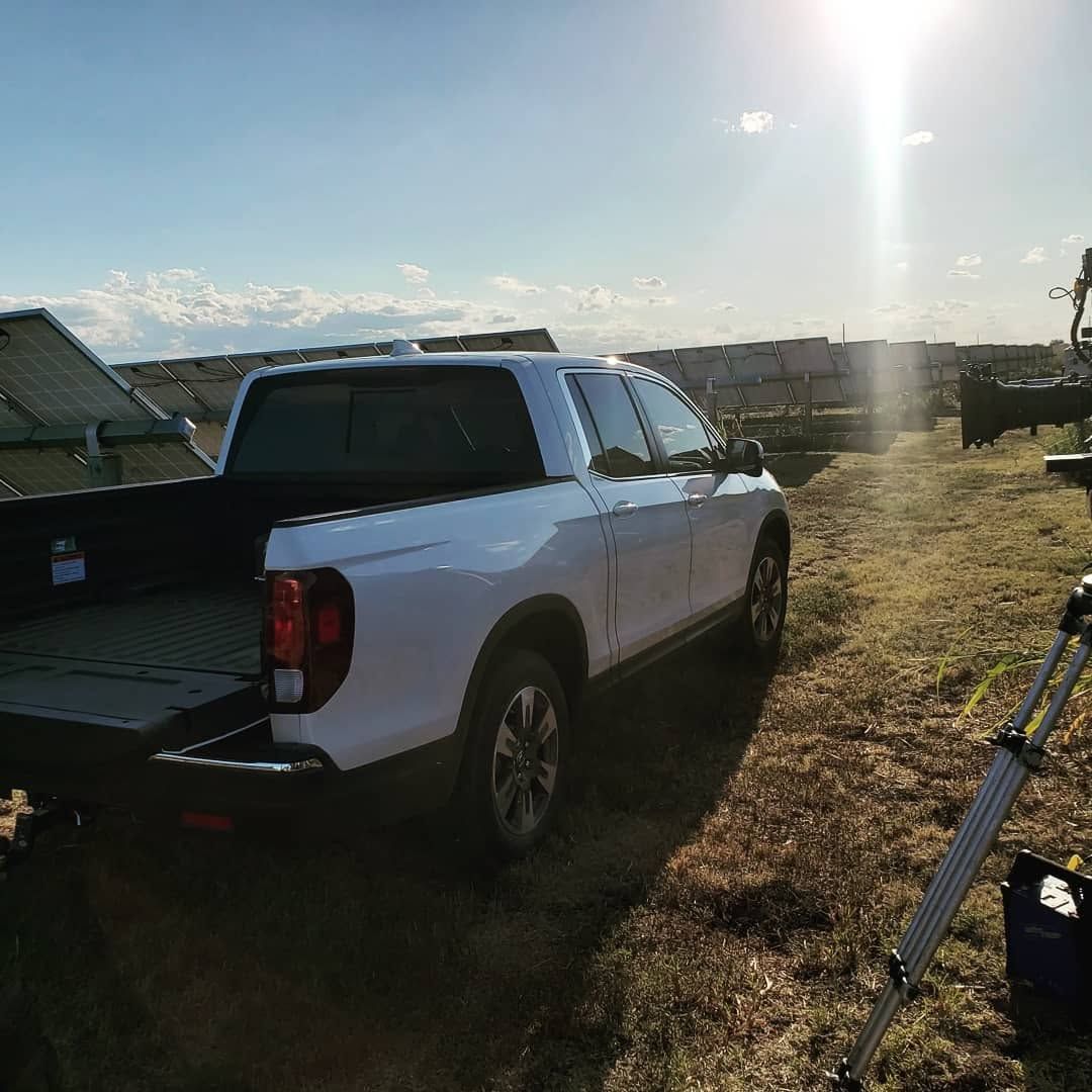 White pickup truck parked in a grassy field at sunset, with a bright sun glare and solar panels nearby