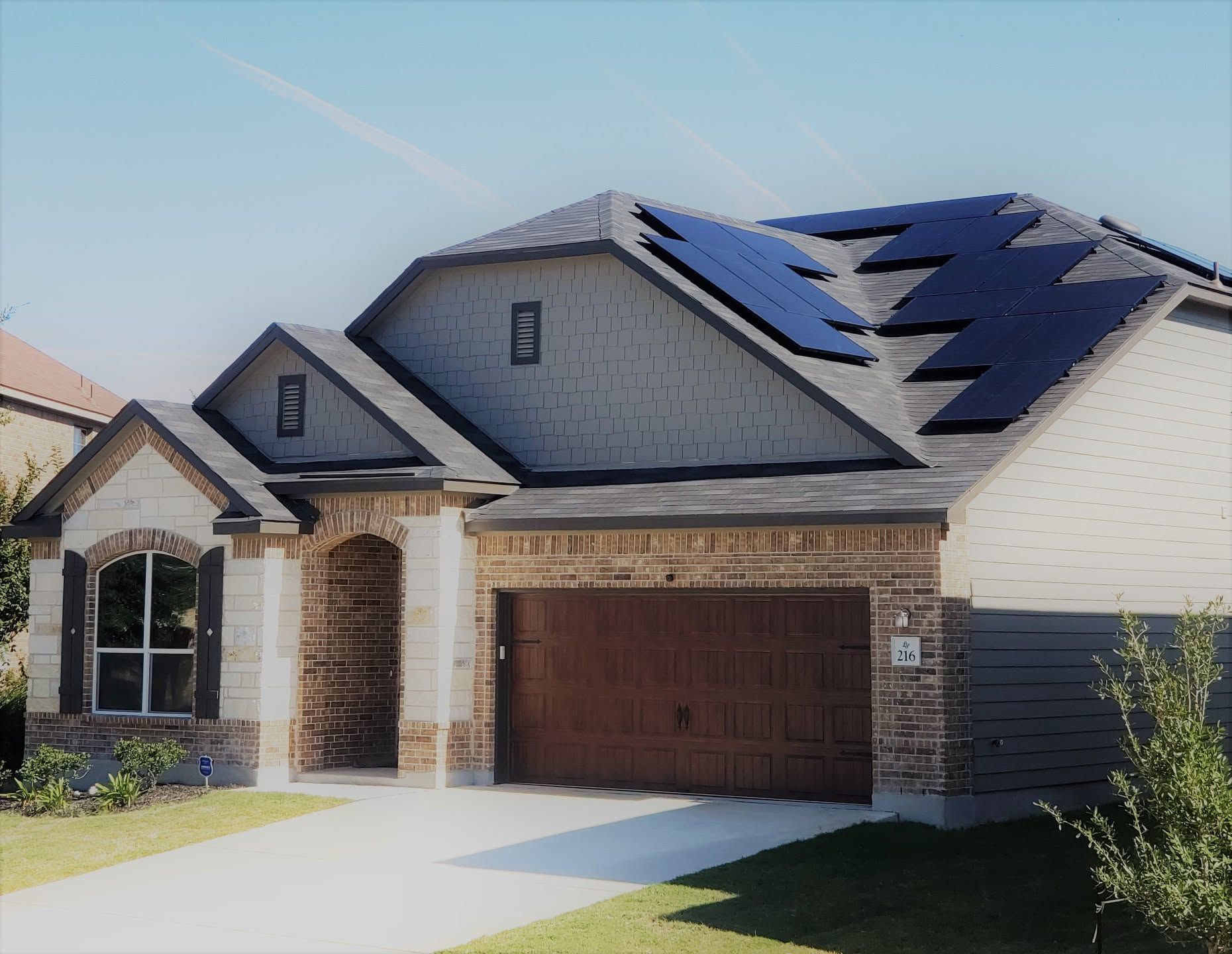 Suburban house exterior with brick garage, white siding, and solar panels on the roof