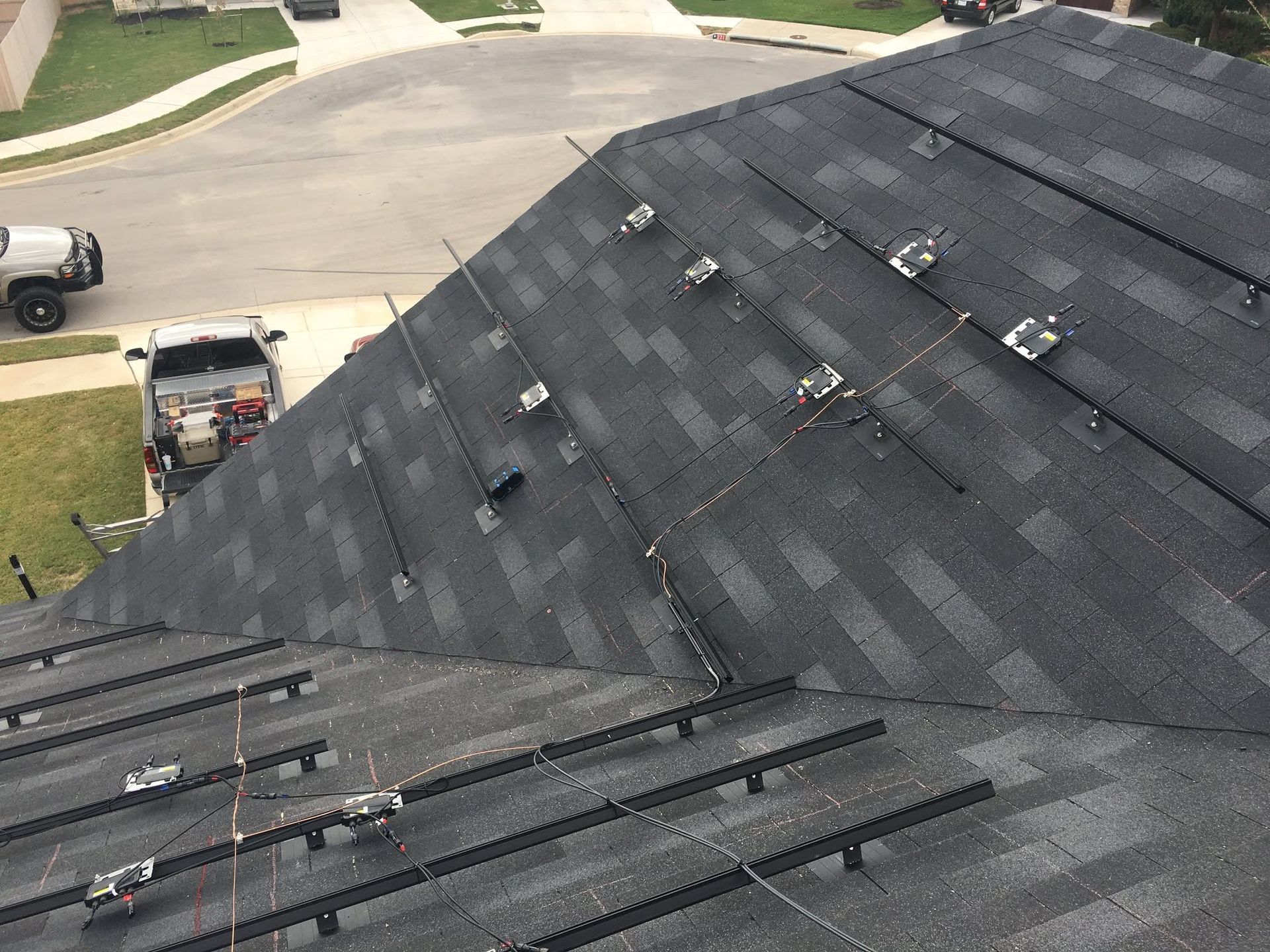 Close-up of a dark shingled roof with roof workers’ equipment and a street visible below