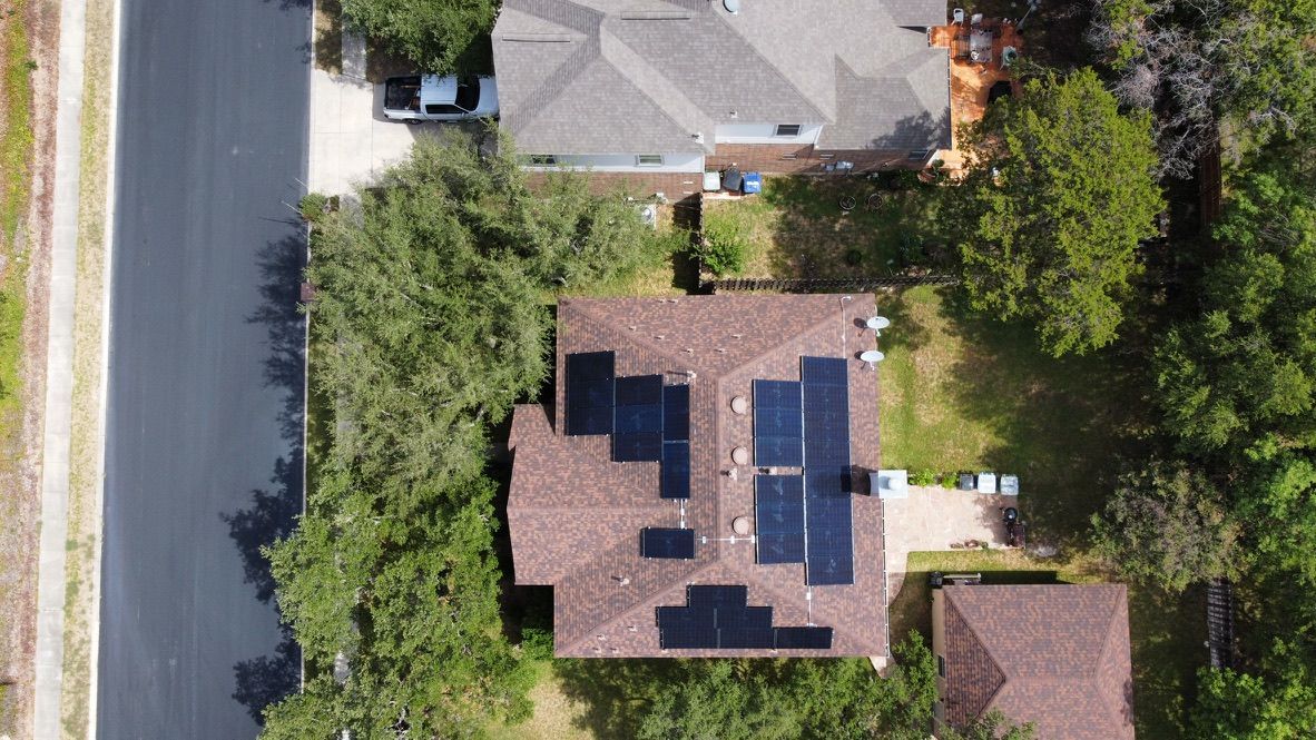 Aerial view of a house with solar panels on the roof beside a road and trees.