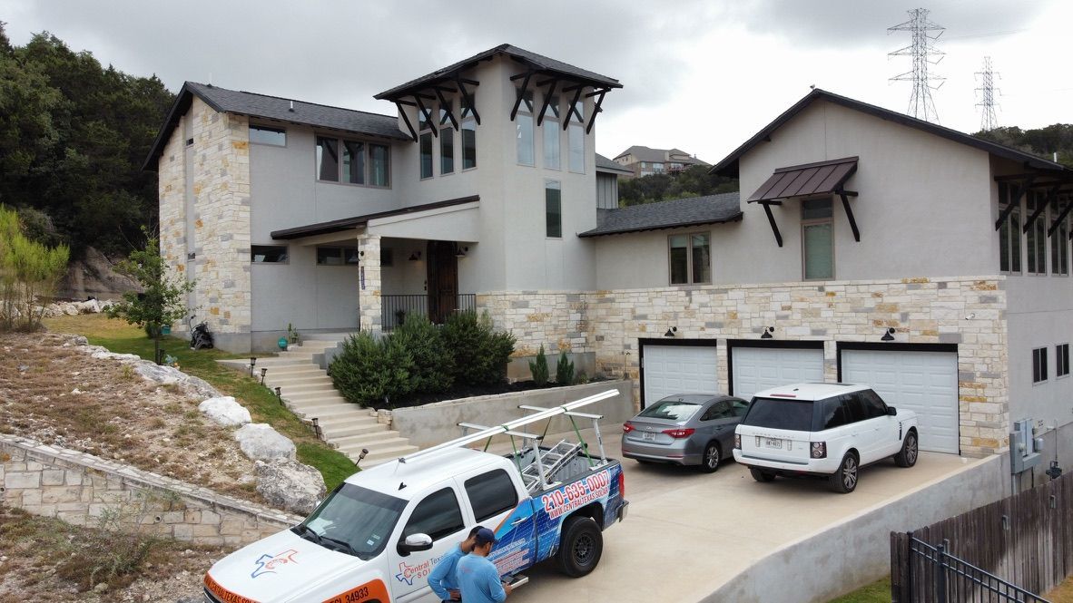 Modern hillside house with stone garage, two cars in driveway, and a pickup truck in front