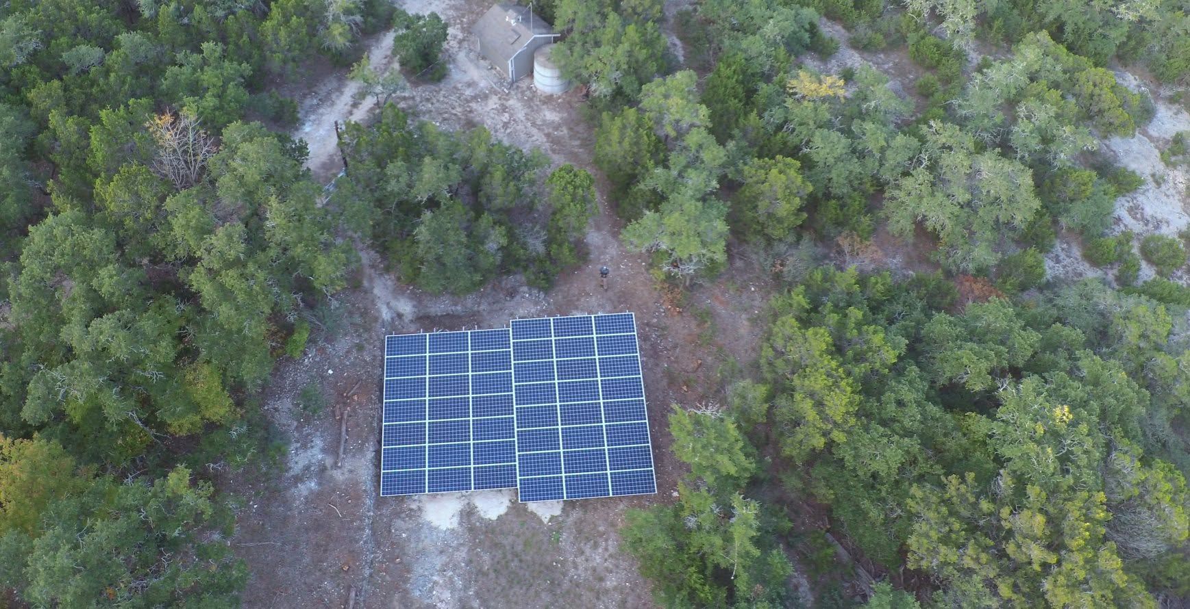 Aerial view of a blue solar panel array surrounded by dense green trees