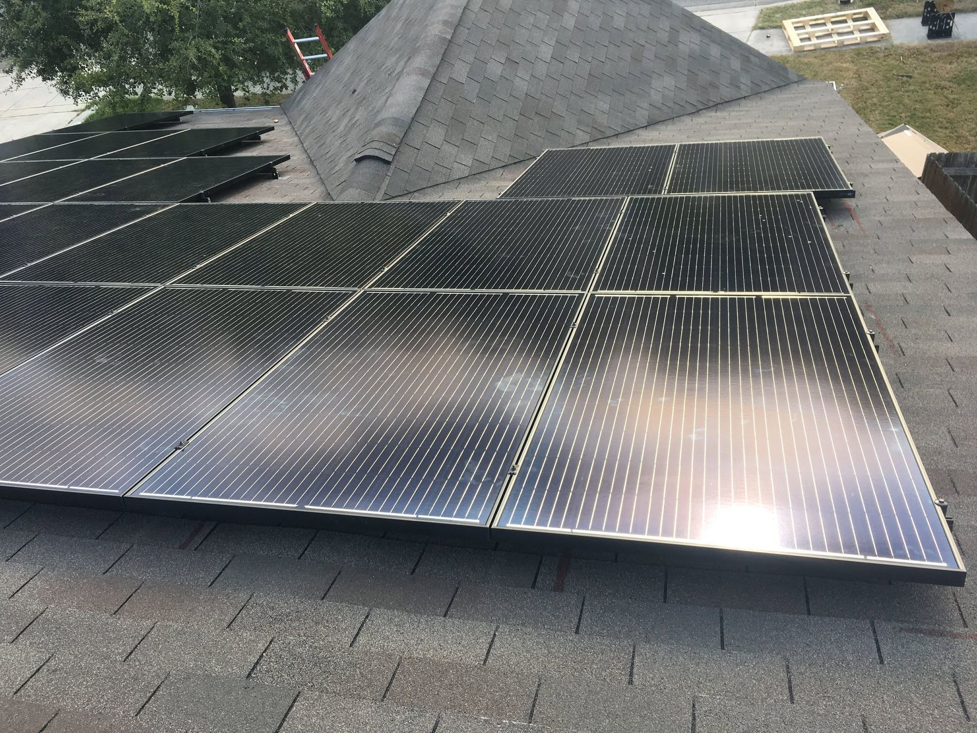 Solar panels mounted on a shingled roof, with a rooftop vent and hillside greenery in the background.