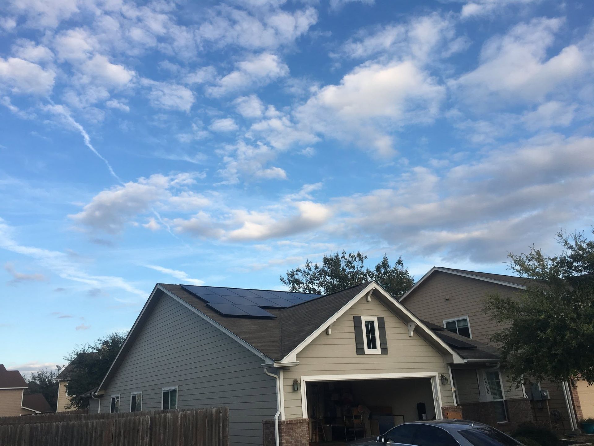 Suburban house with open garage under a partly cloudy blue sky