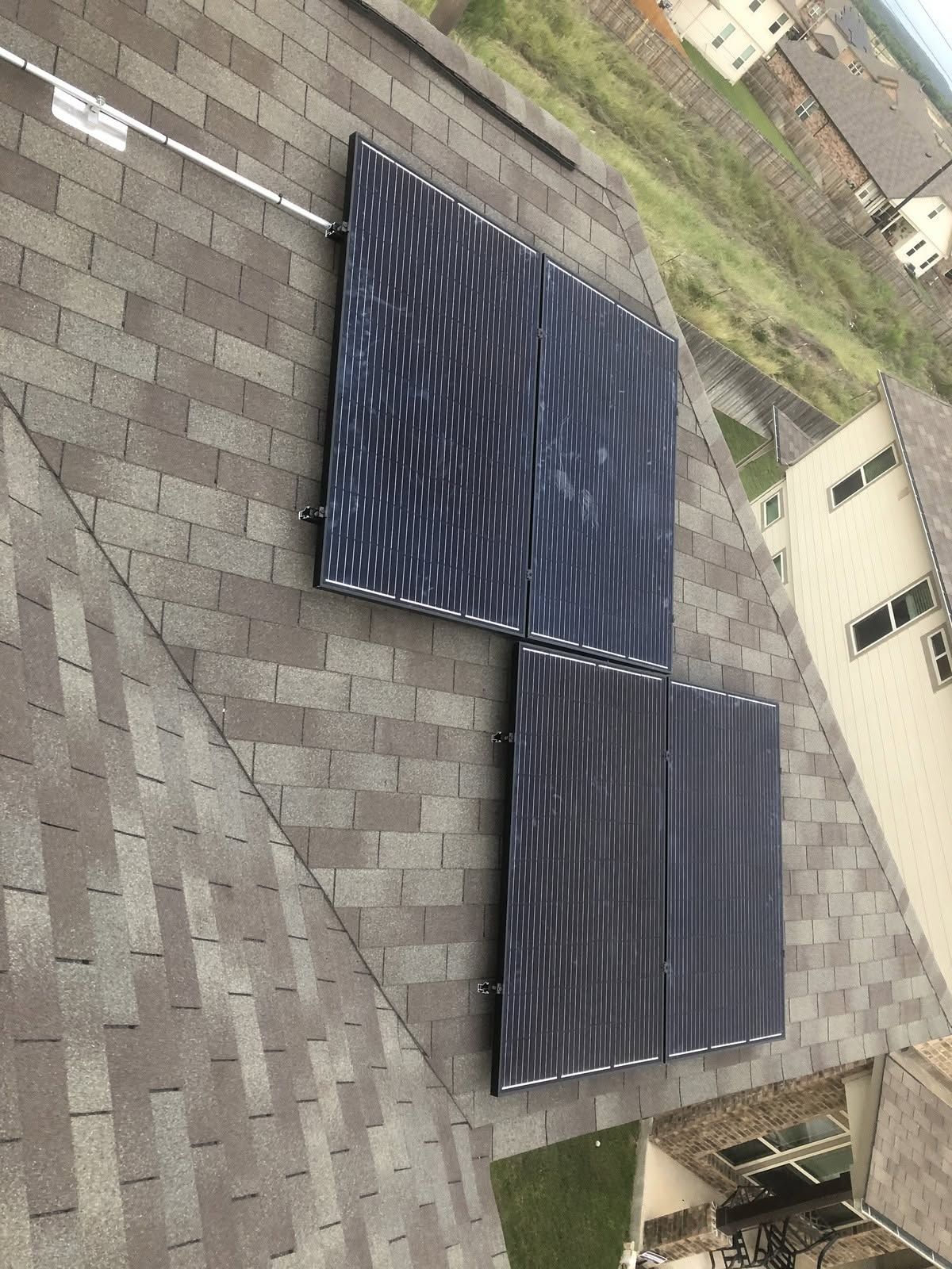 Two dark solar panels mounted on a sloped shingle roof beside a house.
