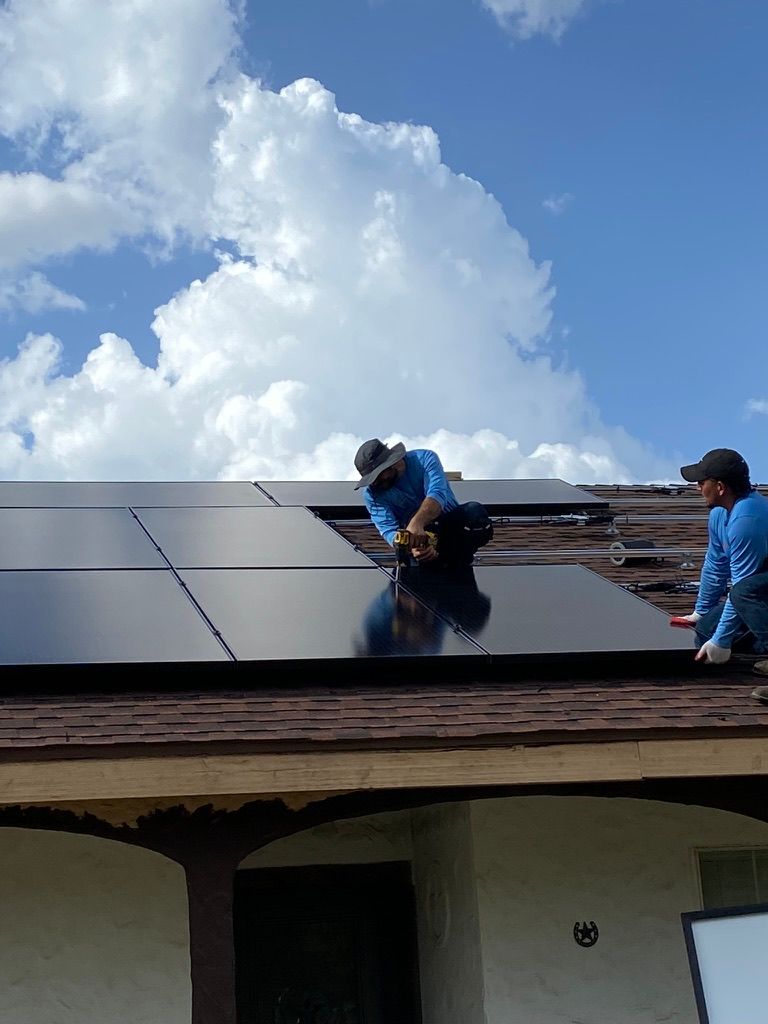 Workers installing solar panels on a roof under a partly cloudy sky