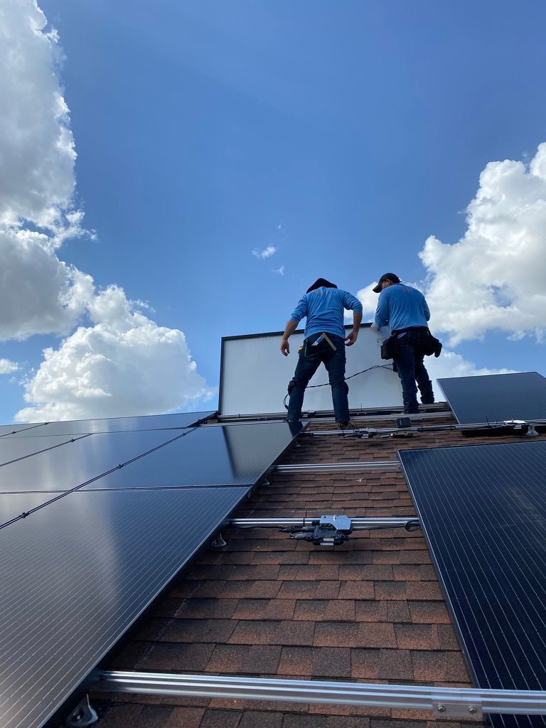 Two workers installing solar panels on a steep roof under a blue sky