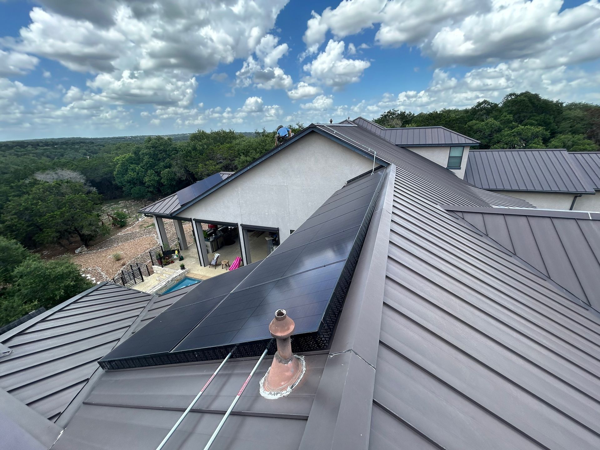 Rooftop with solar panels on a metal roof, overlooking trees and a cloudy sky