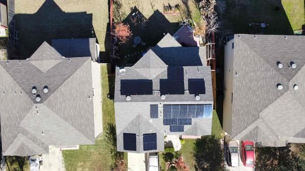 Aerial view of three suburban houses, with solar panels on the center roof and cars in driveways.