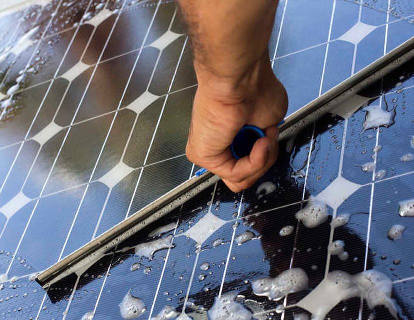 Hand cleaning a solar panel with soap suds and a squeegee