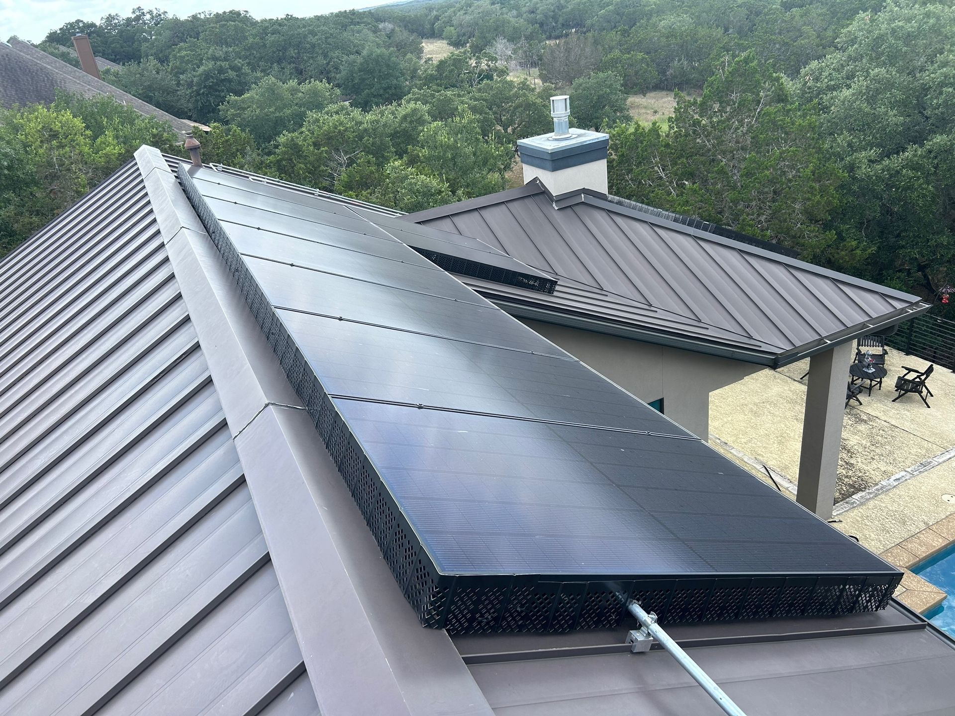 Solar panels mounted on a gray metal roof with a wooded hillside in the background
