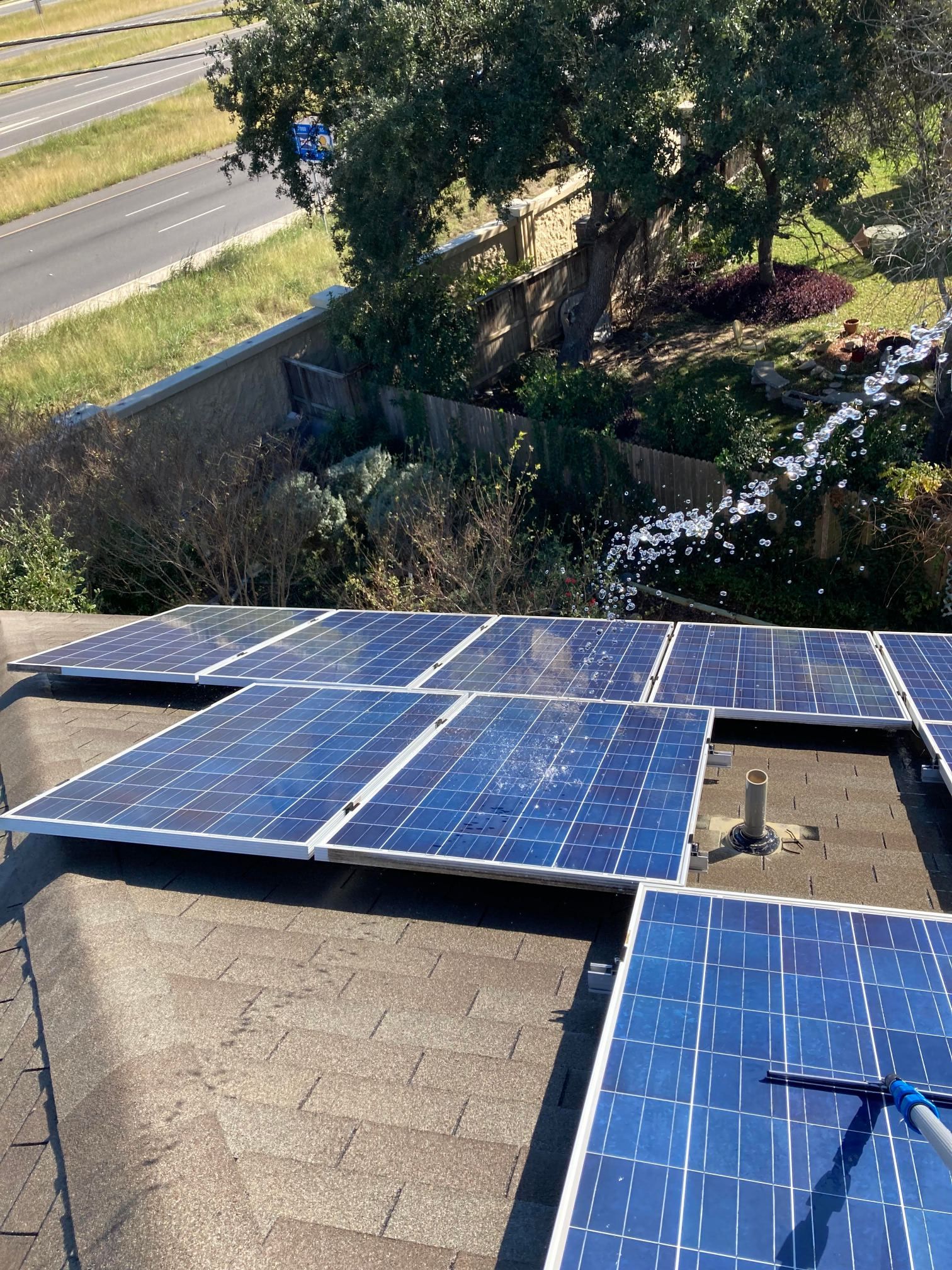 Rooftop with blue solar panels beside trees and a roadway