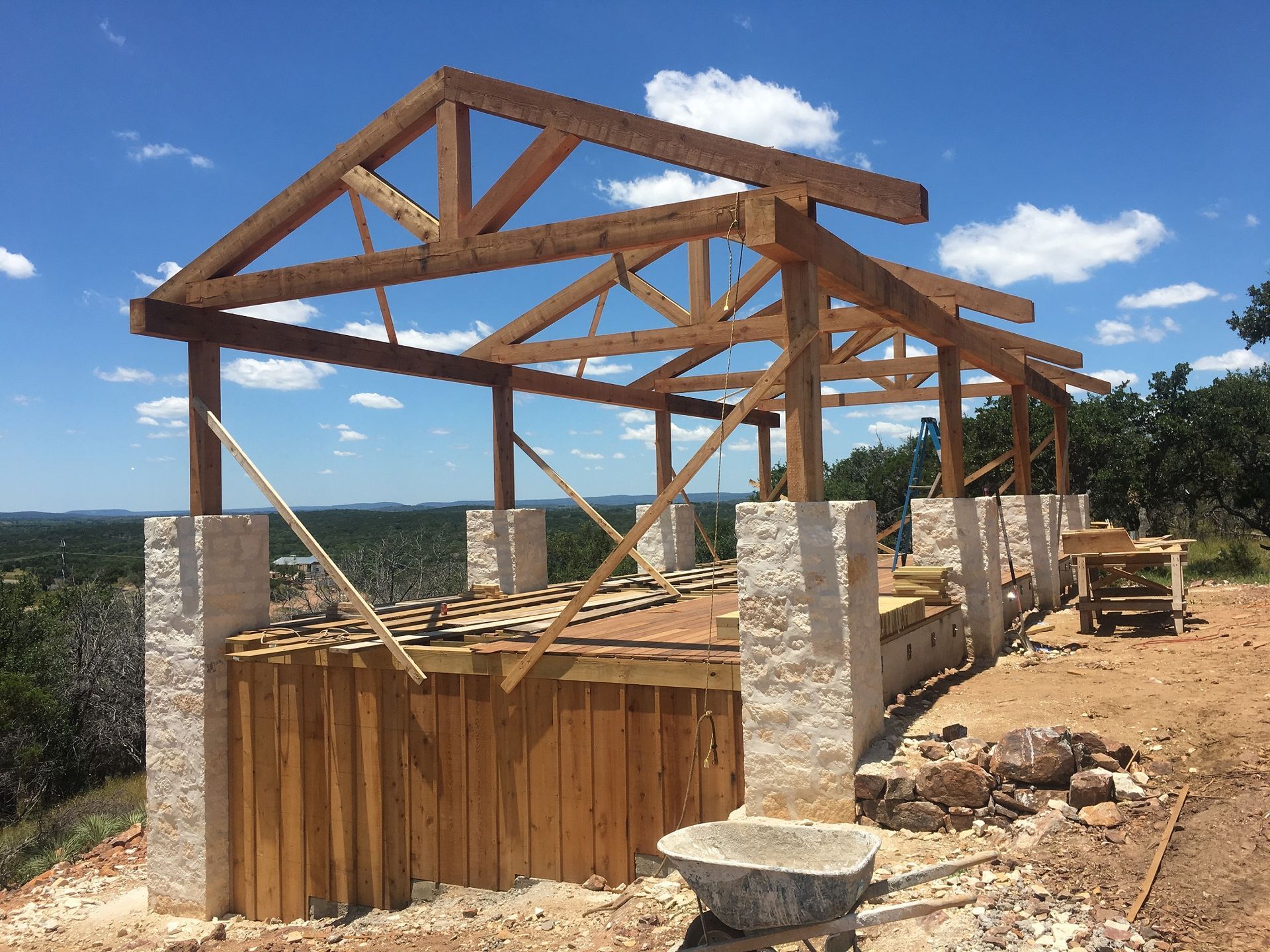 Partially built wooden house frame on stone columns under a blue sky.