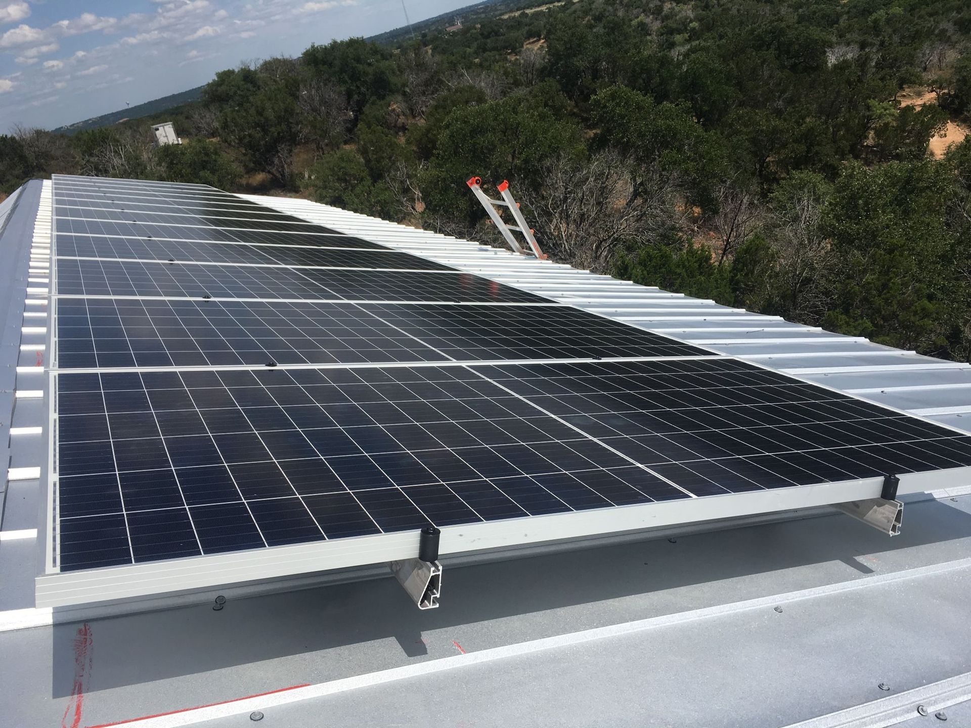 Solar panels mounted on a rooftop with a forested hillside in the background.