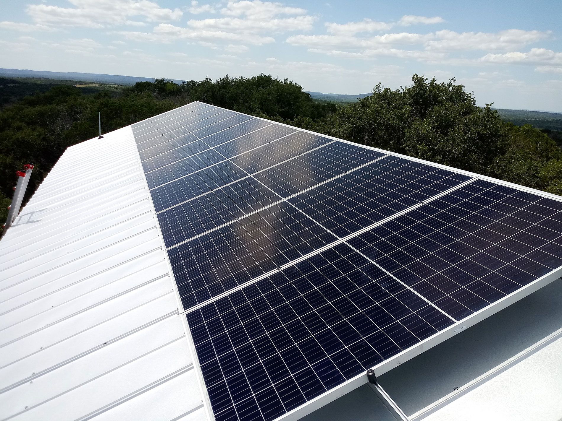Solar panels on a rooftop with trees and sky in the background.