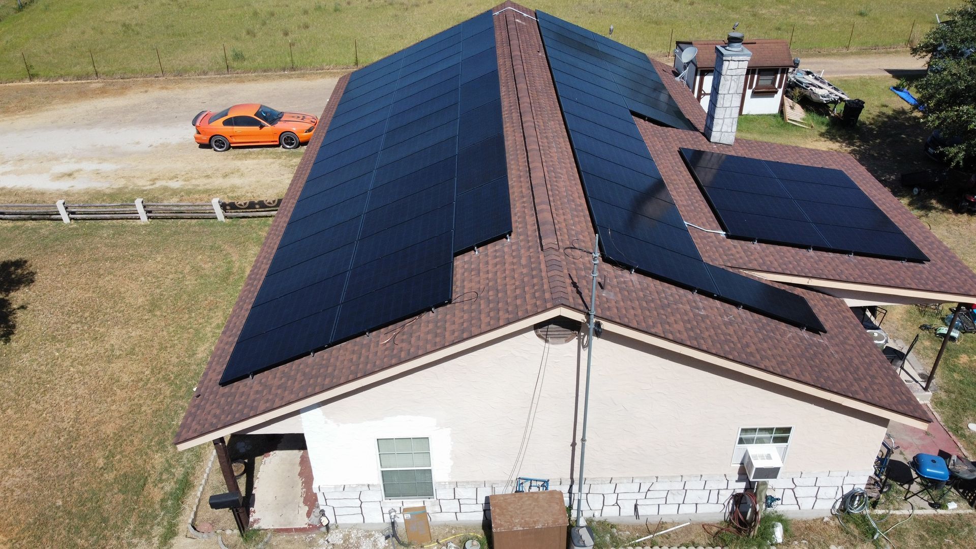 Aerial view of a house roof covered with solar panels beside a driveway and orange car.
