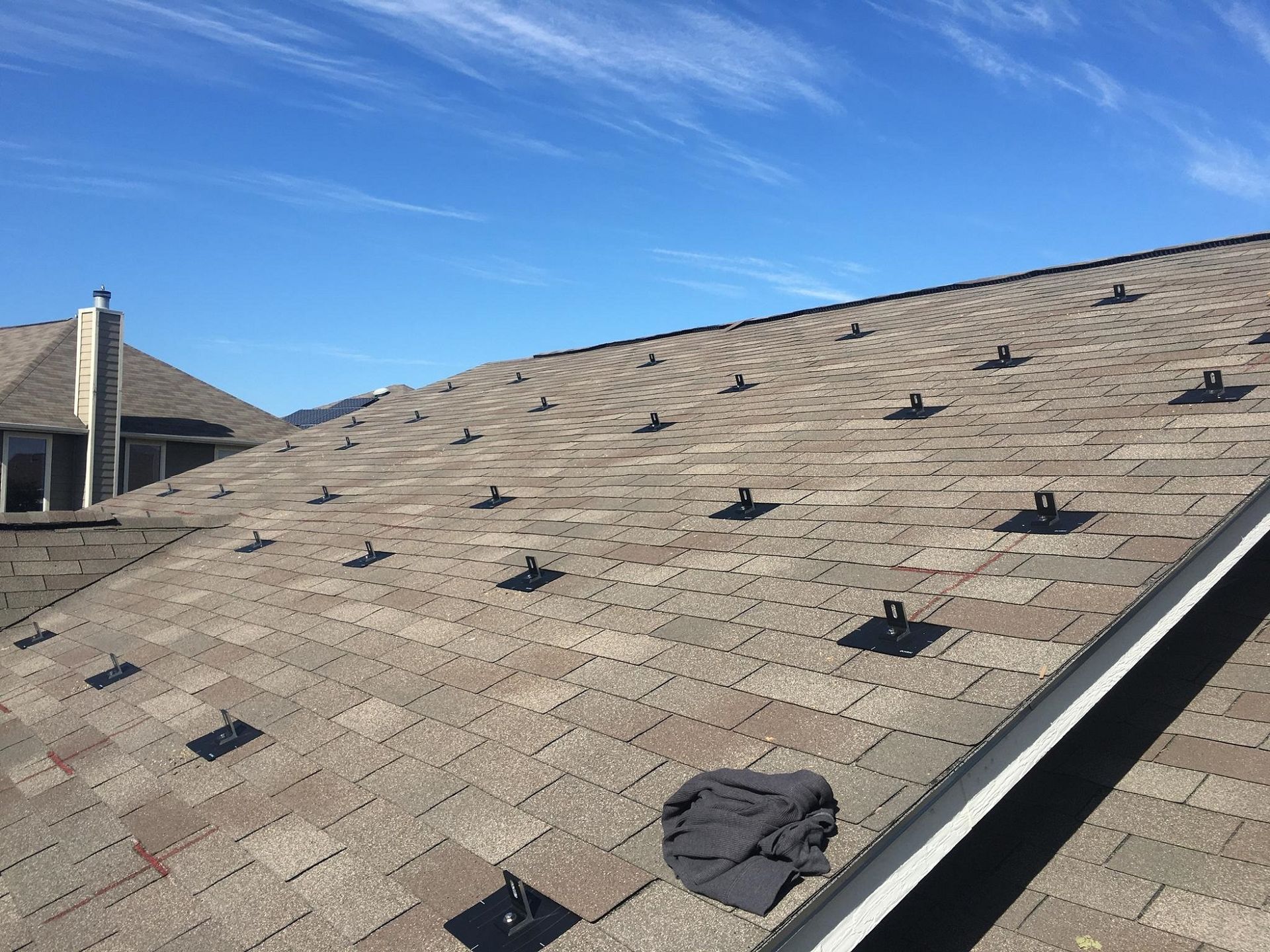 Rooftop with gray shingles, scattered roof vents, and a small dark patch near the edge under a blue sky