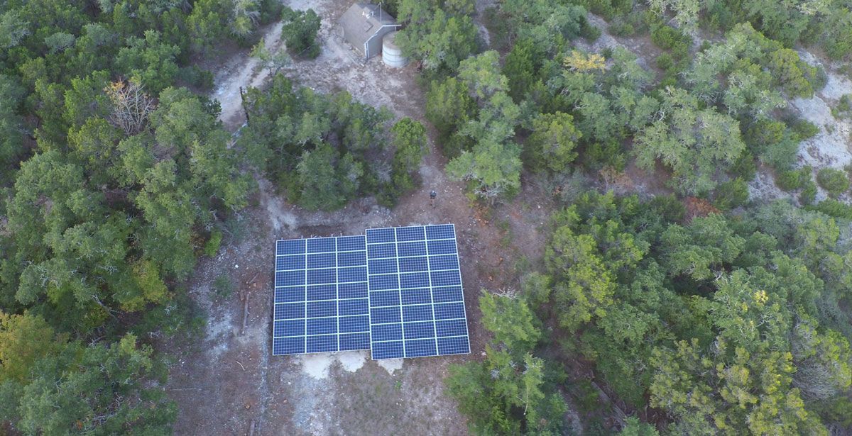 Aerial view of blue solar panels set in a forest clearing.
