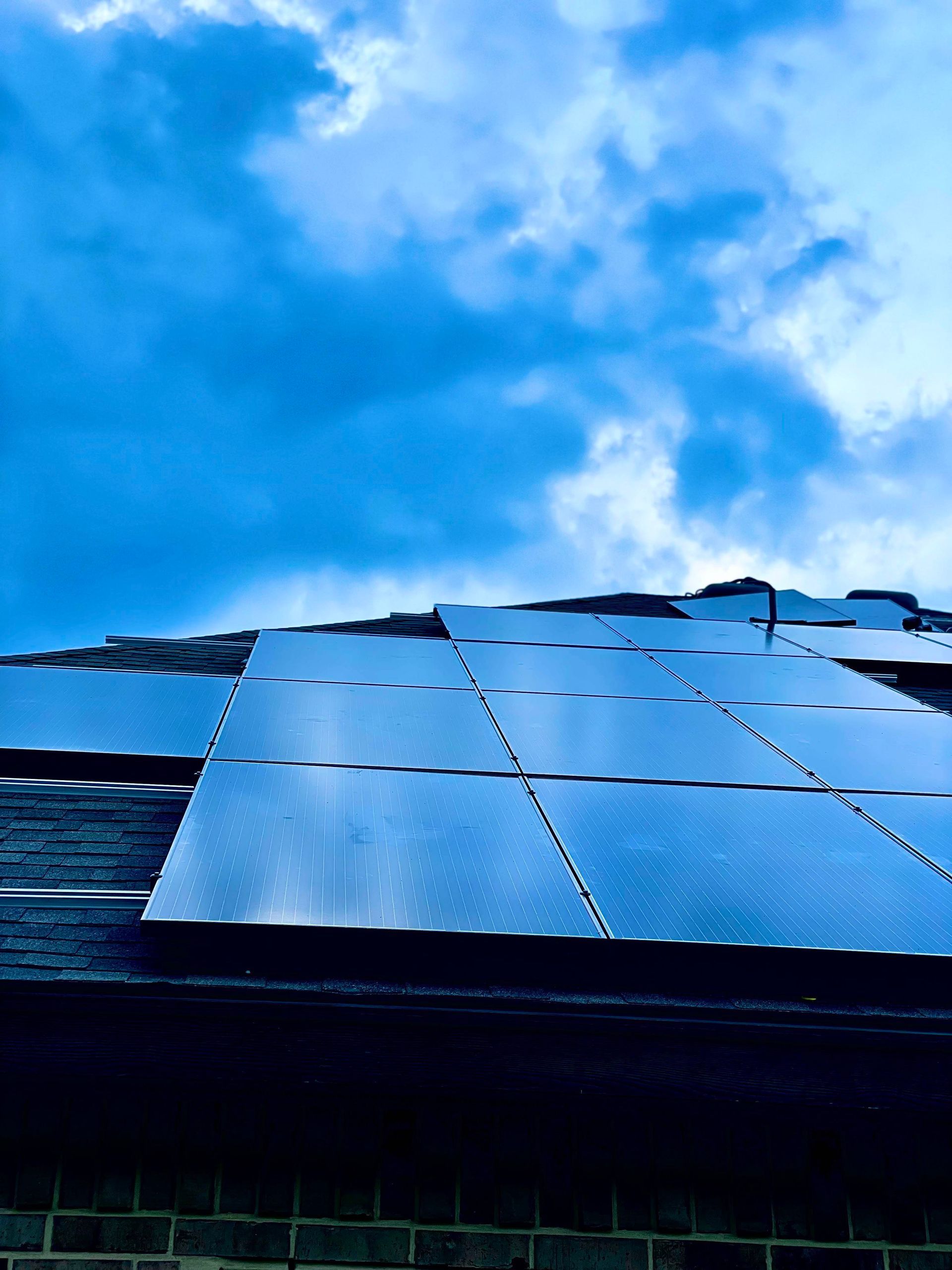 Blue solar panels against a bright blue sky with clouds