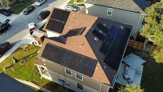 Aerial view of a house roof with solar panels and parked cars along the street