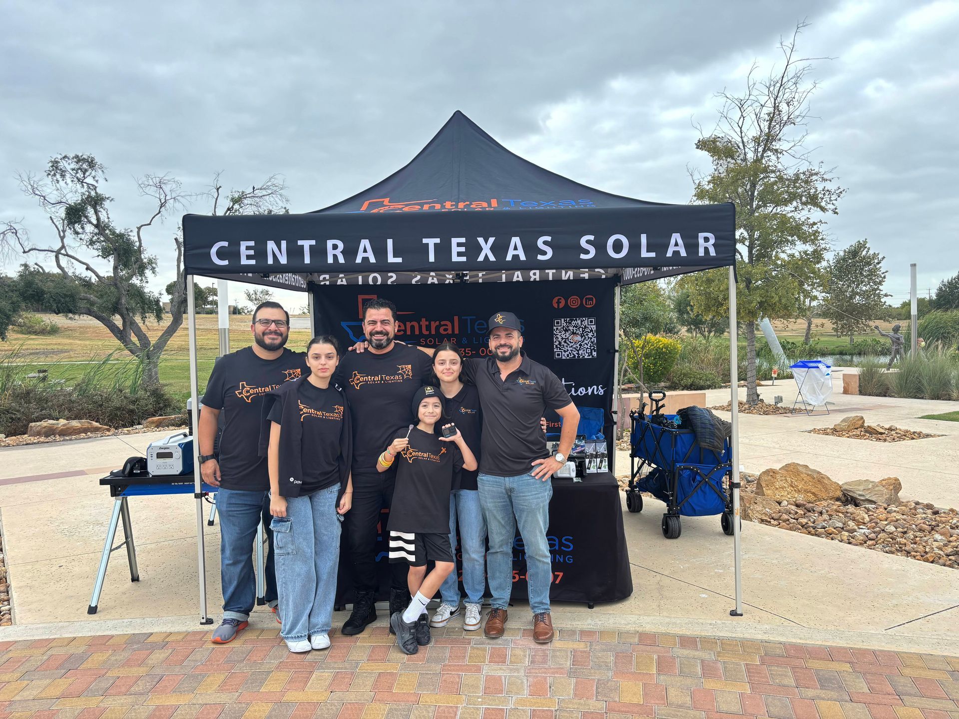 Five people pose under a Central Texas Solar canopy at an outdoor event booth.