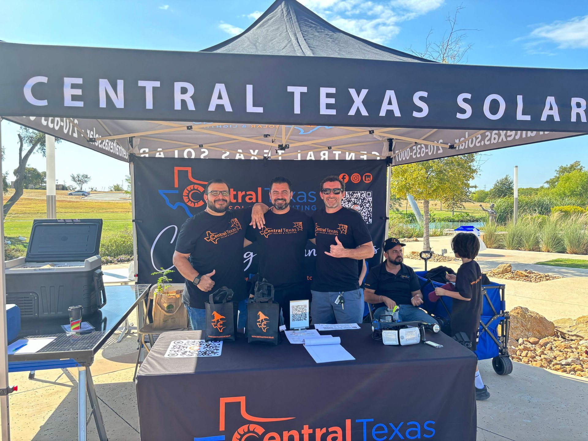 Central Texas Solar team at an outdoor booth under a black canopy, posing beside branded tables and equipment