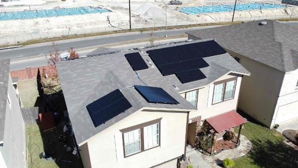 Aerial view of a house with dark roof tiles and solar panels in a suburban neighborhood