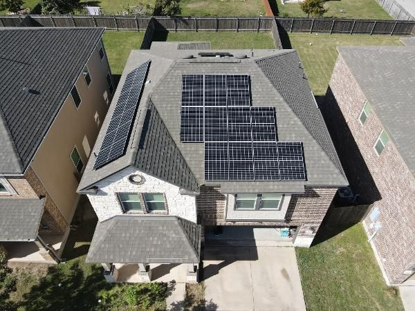 Aerial view of a house with solar panels on the roof, surrounded by neighboring homes and a fenced yard.