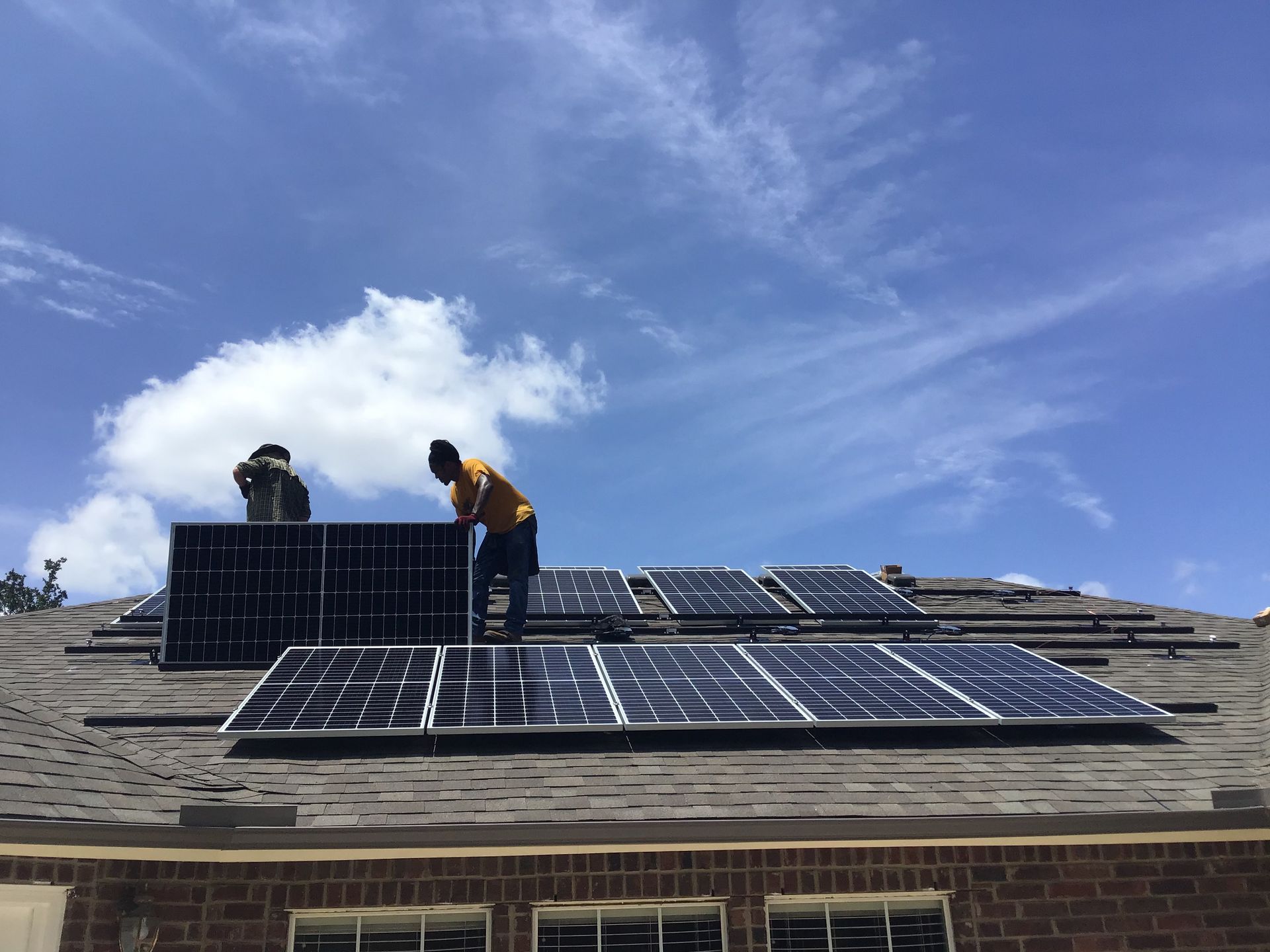 Workers installing solar panels on a rooftop under a blue sky