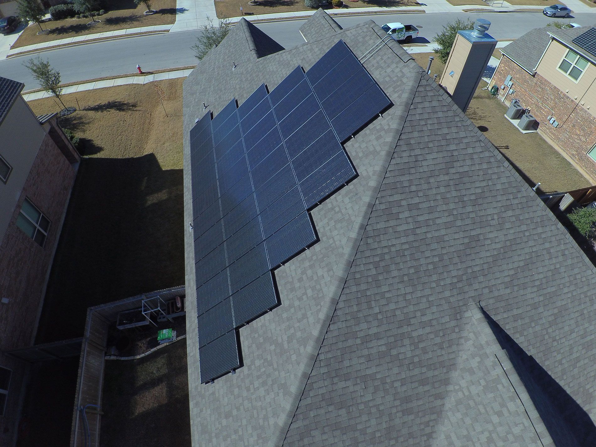 Solar panels on a gray shingled roof in a suburban neighborhood.