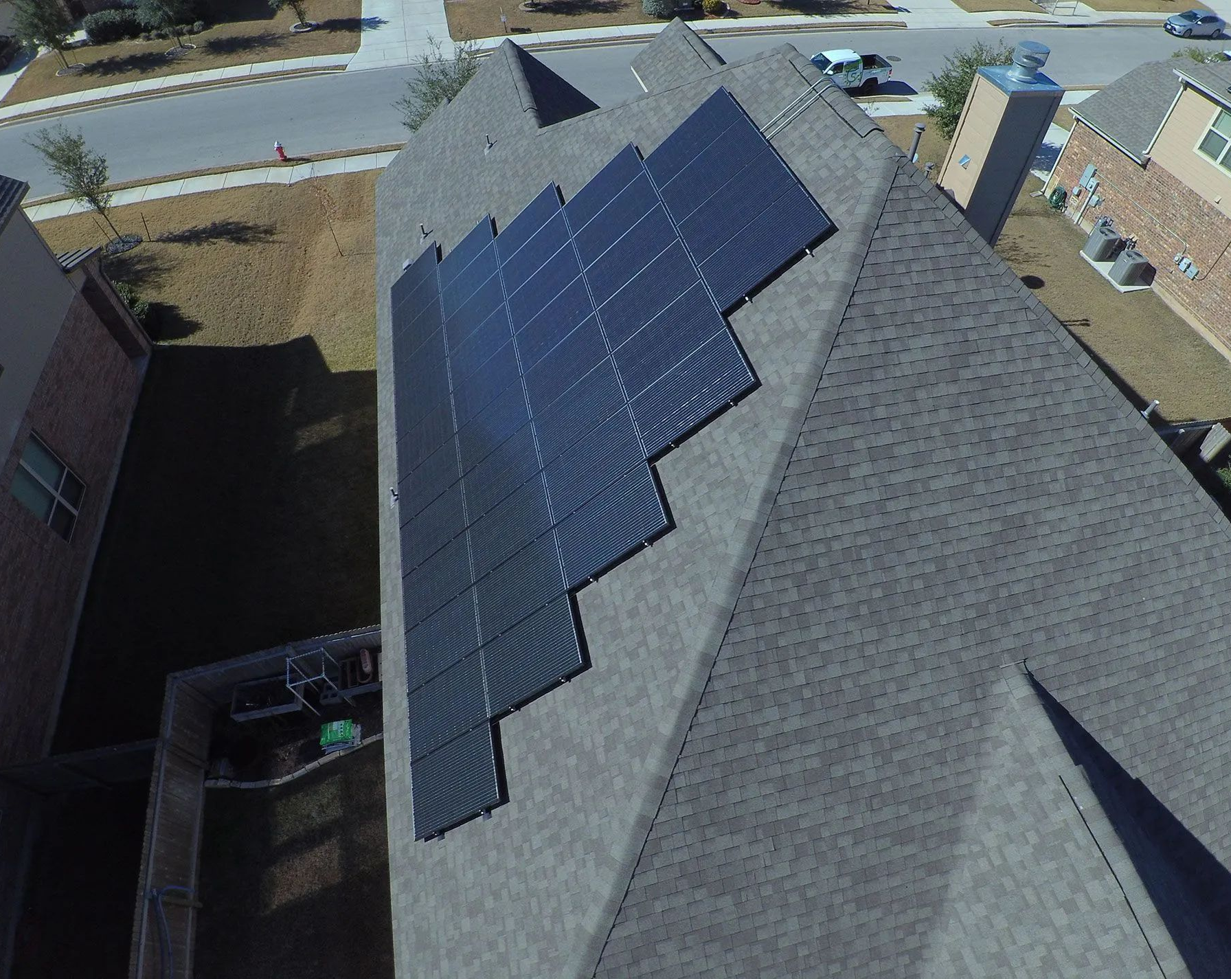Aerial view of a house roof with dark solar panels installed on one side.