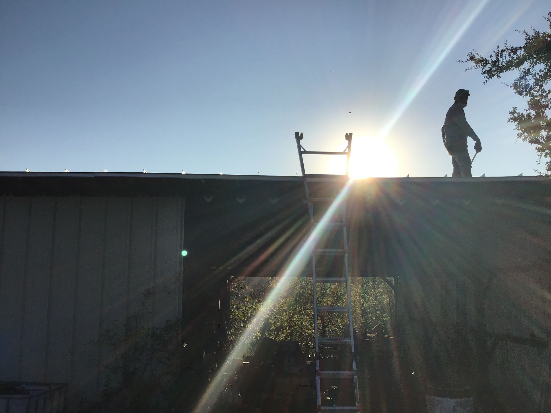 Silhouette of a person on a rooftop at sunset, with bright sun rays and a ladder below.