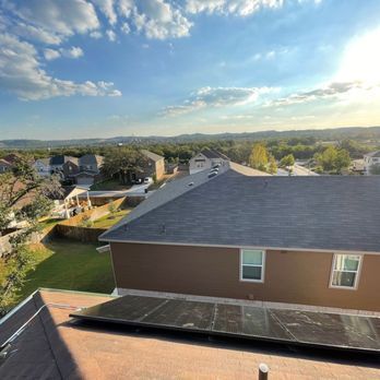Rooftop with rows of dark solar panels on gray shingles in a residential neighborhood