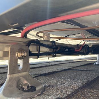 Underside of a device with red and black wires secured to a metal bracket on a roof surface