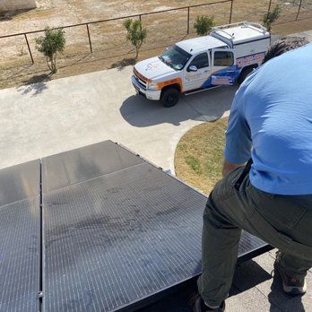 Worker on a rooftop near a white utility truck parked below.
