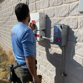 Technician opening an outdoor electrical meter box on a stone wall.