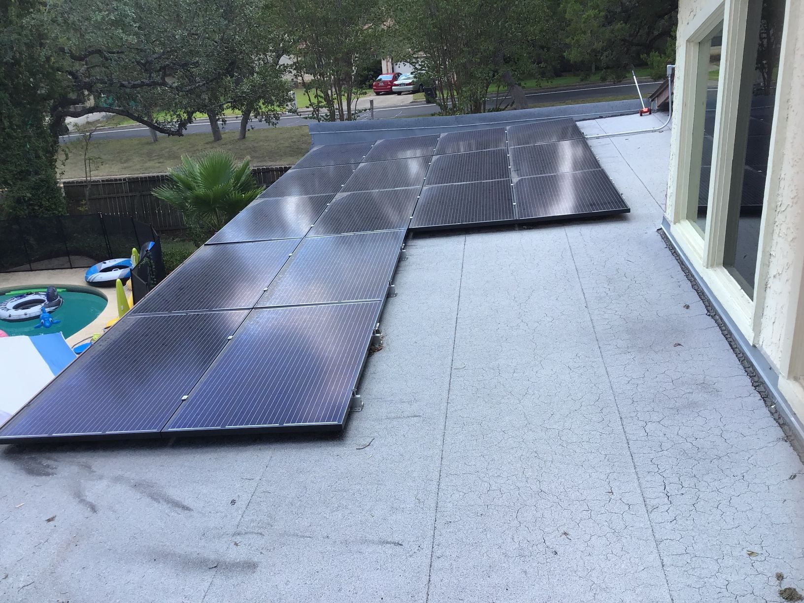 Solar panels lined across a flat rooftop beside windows and trees in the background