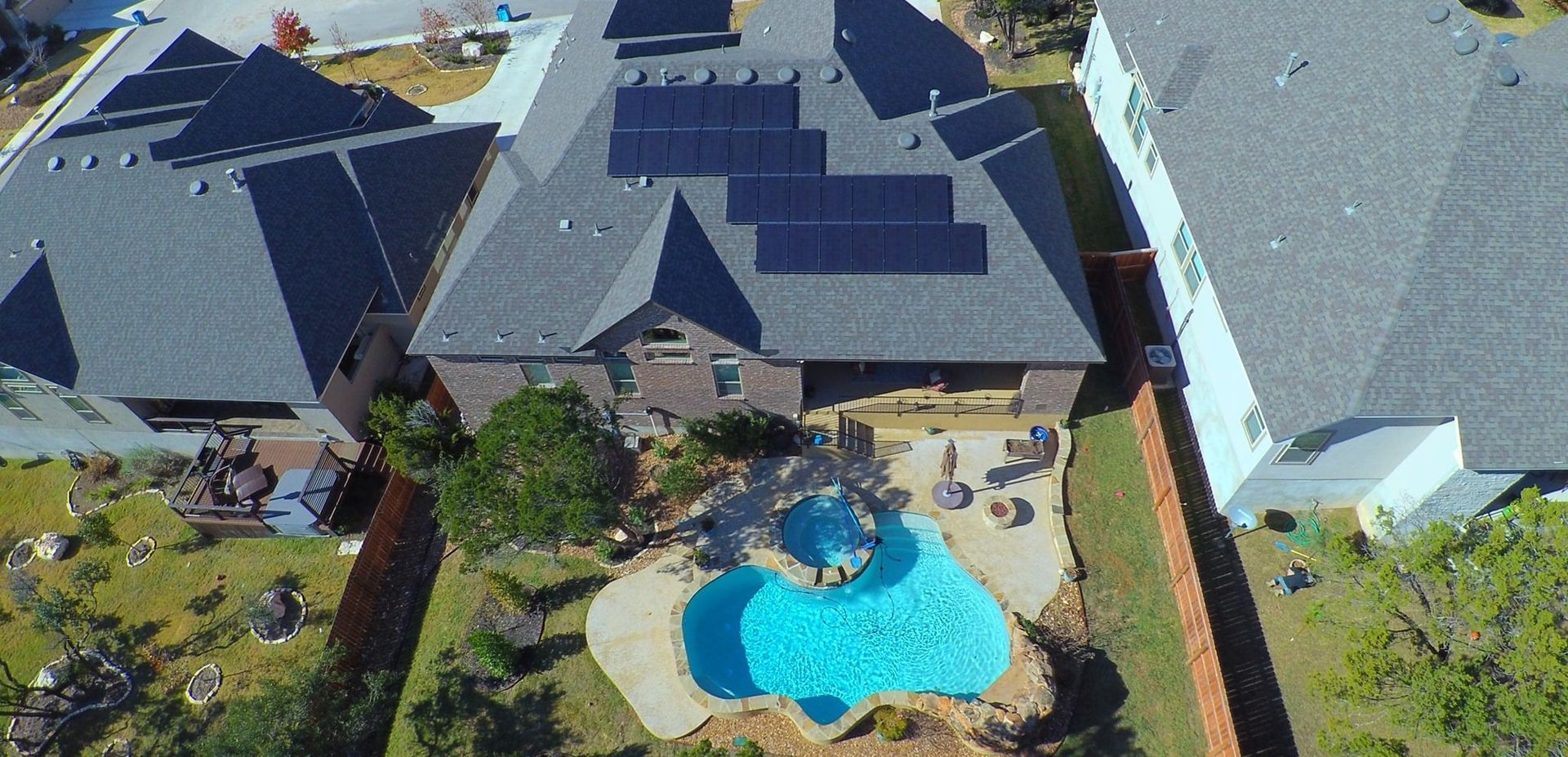 Aerial view of a suburban house with solar panels and a backyard swimming pool