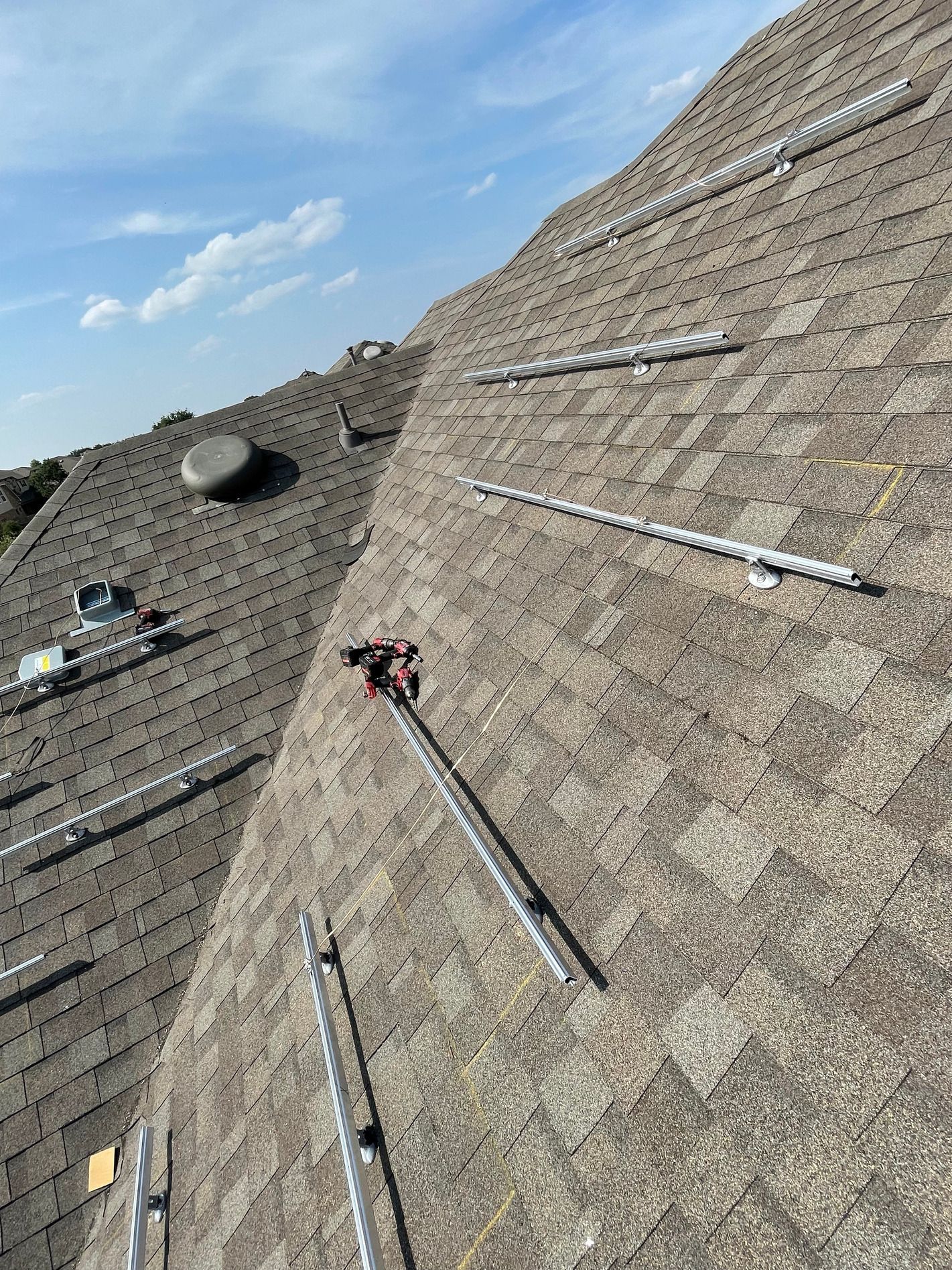 Roof with gray shingles, solar panels, and roof-mounted equipment under a blue sky