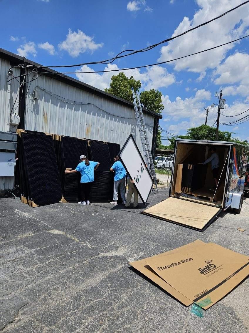 Two workers moving black panels beside a truck in an outdoor lot under a blue sky