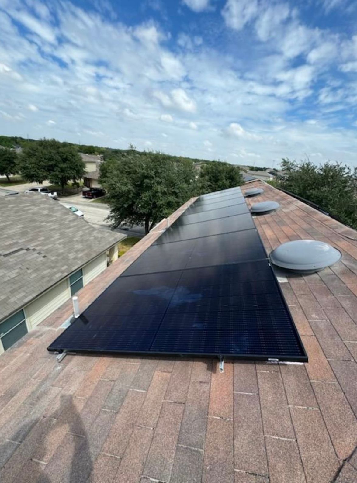 Solar panels on a shingled rooftop under a partly cloudy sky.