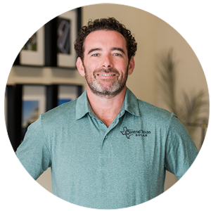 Smiling man in a teal polo shirt standing indoors in front of framed wall art.