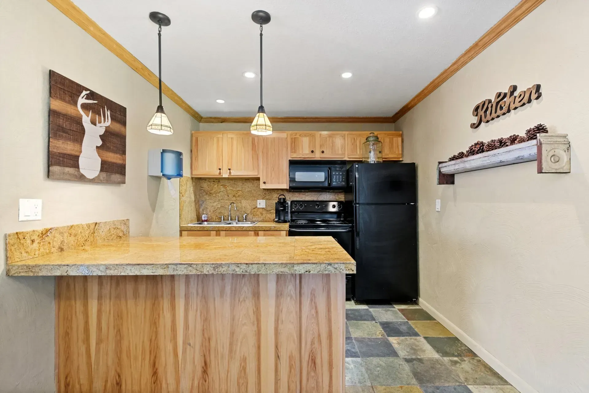Cozy kitchen with wood cabinets, black appliances, granite counter, pendant lights, and deer wall art.